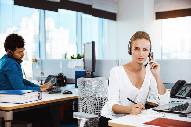 Giovane bello operatore telefonico femminile di sostegno che parla, consultando, sopra l'ufficio