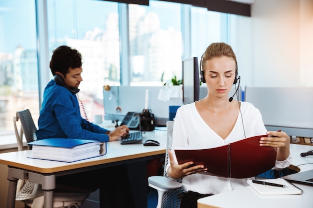 Giovane bello operatore telefonico femminile di sostegno che parla, consultando, sopra l'ufficio