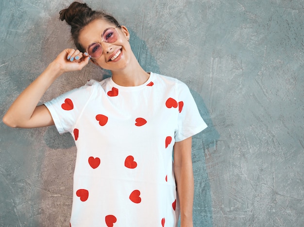 Giovane bello sguardo sorridente della donna. Ragazza alla moda in abito bianco estivo casual e occhiali da sole.