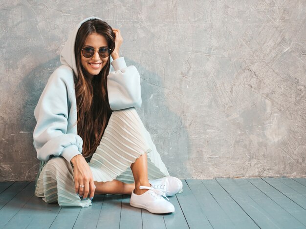 Giovane bello sguardo sorridente della donna. Ragazza alla moda in felpa estiva casual e abiti gonna. sedendo sul pavimento