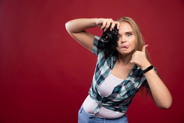 Giovane bionda fotografa in possesso di una macchina fotografica professionale e si fa il selfie in strane posizioni.