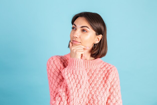 Giovane bruna in caldo maglione rosa isolato sulla parete blu