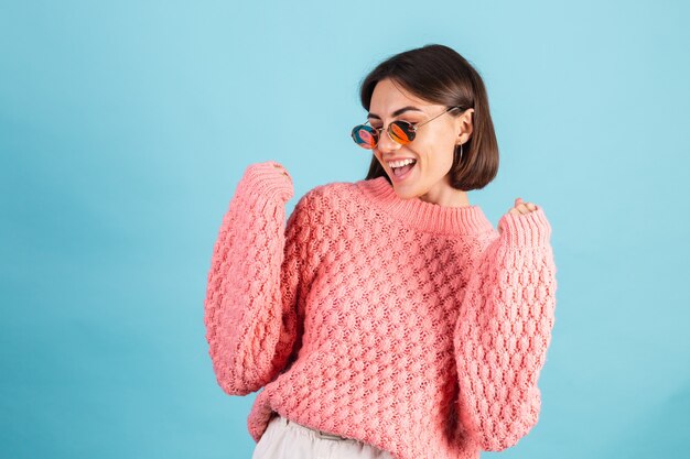 Giovane bruna in caldo maglione rosa isolato sulla parete blu