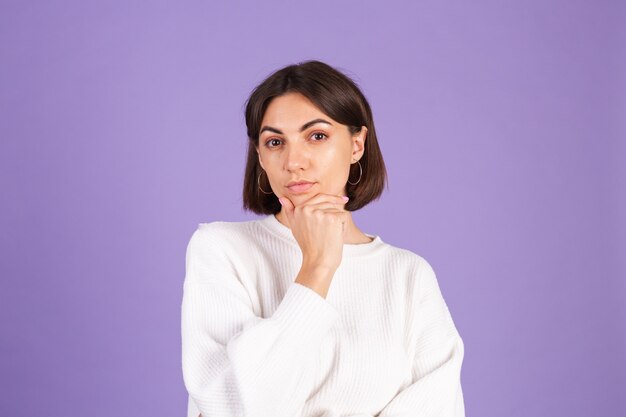 Giovane bruna in maglione casual bianco isolato sulla parete viola