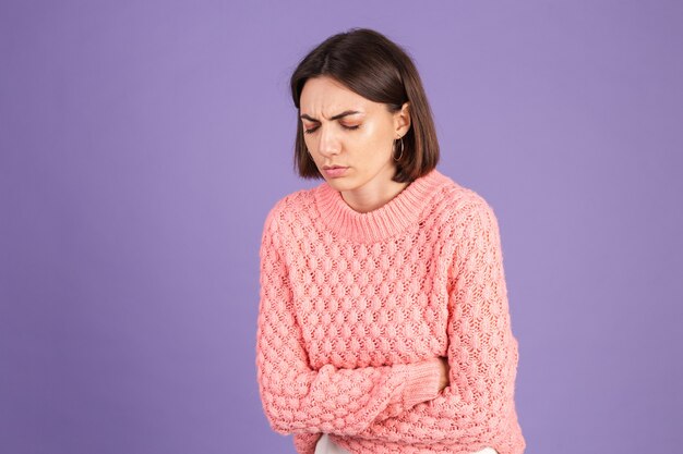 Giovane bruna in maglione rosa isolato sulla parete viola