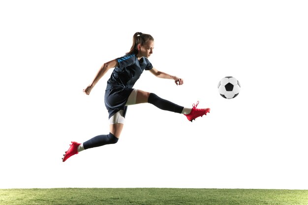 Giovane calcio femminile o giocatore di football con i capelli lunghi in abbigliamento sportivo e stivali calciare la palla per l'obiettivo nel salto isolato su sfondo bianco. Concetto di stile di vita sano, sport professionistico, hobby.