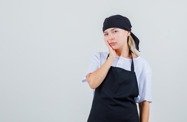 Giovane cameriera che ha mal di denti in uniforme e grembiule e sembra triste