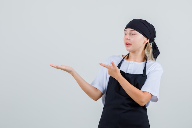 Giovane cameriera in uniforme e grembiule che punta al palmo aperto