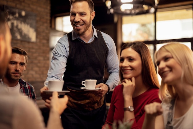 Giovane cameriere felice che dà caffè ai suoi clienti mentre li serve in una caffetteria