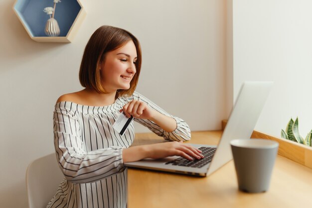 Giovane carta di credito femminile felice della tenuta e per mezzo del computer portatile.