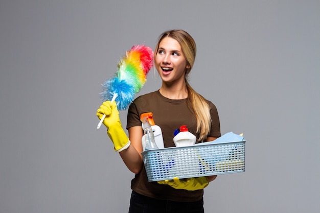 Giovane casalinga attraente che indossa abiti casual, guanti in lattice che tengono una bacinella piena di detergente isolato su bianco