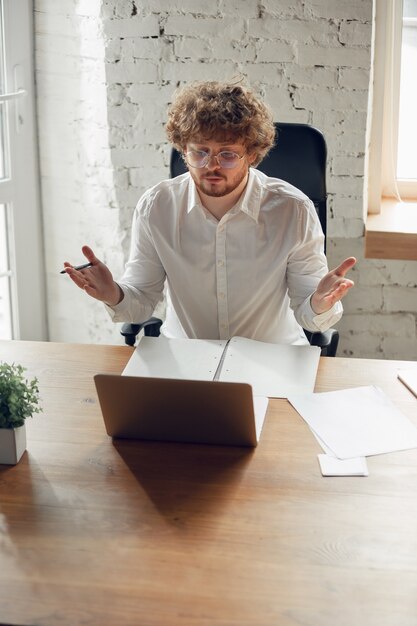 Giovane caucasico in abbigliamento d'affari che lavora in ufficio, lavoro, studio online