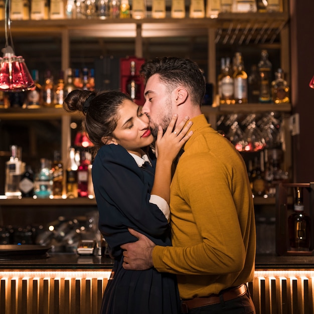 Giovane che abbraccia e che bacia donna affascinante al bancone del bar