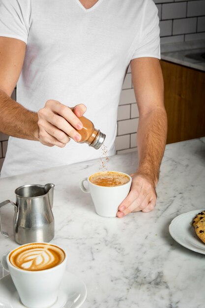 Giovane che aggiunge cannella in una tazza di cappuccino