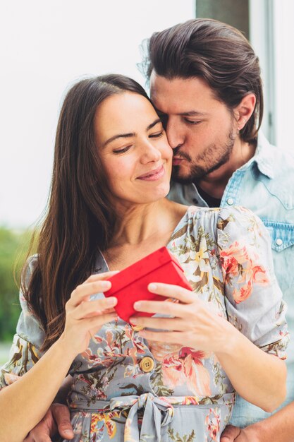 Giovane che bacia donna con regalo sulla guancia