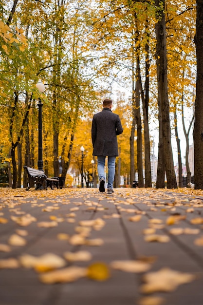 Giovane che cammina nella città d'autunno con un bicchiere di caffè