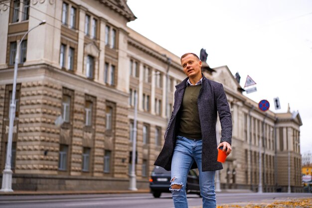 Giovane che cammina nella città d'autunno con un bicchiere di caffè