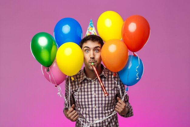 Giovane che celebra il compleanno, tenendo baloons colorati sul muro viola.