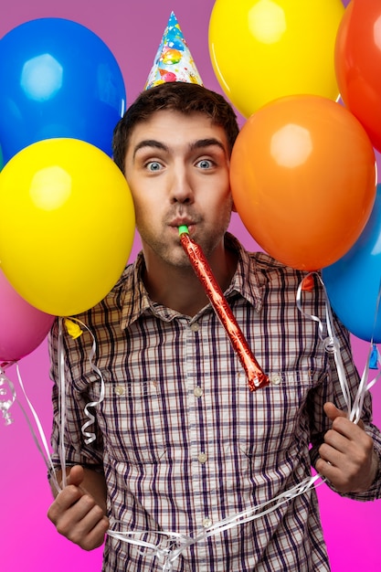 Giovane che celebra il compleanno, tenendo baloons colorati sul muro viola.