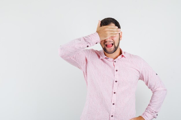 Giovane che copre gli occhi con la mano in camicia rosa e guardando eccitato