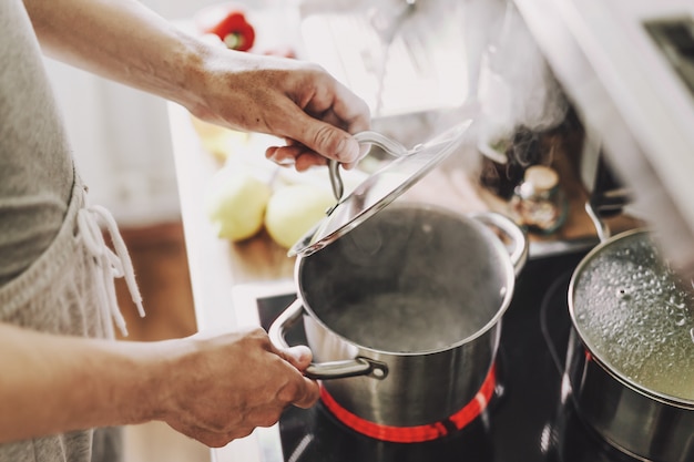 Giovane che cucina alimento fresco a casa e che apre coperchio della pentola di cottura a vapore.