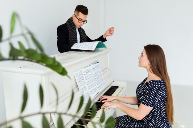 Giovane che esamina lo strato musicale che assiste la donna che gioca piano