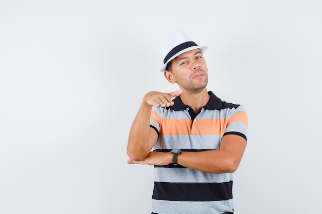 Giovane che gesticola come rendere piatto in t-shirt e cappello e guardando consapevole