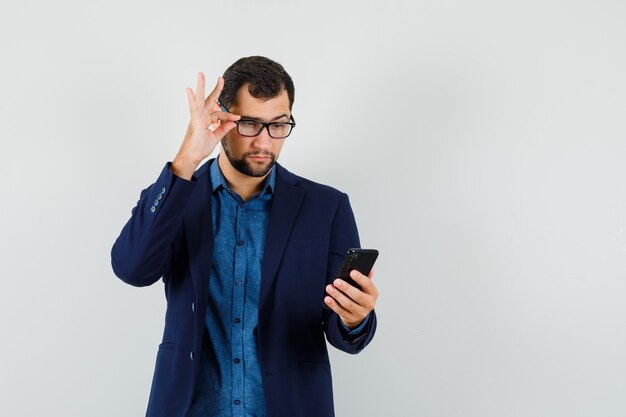 Giovane che guarda attentamente il telefono cellulare in camicia, vista frontale giacca.