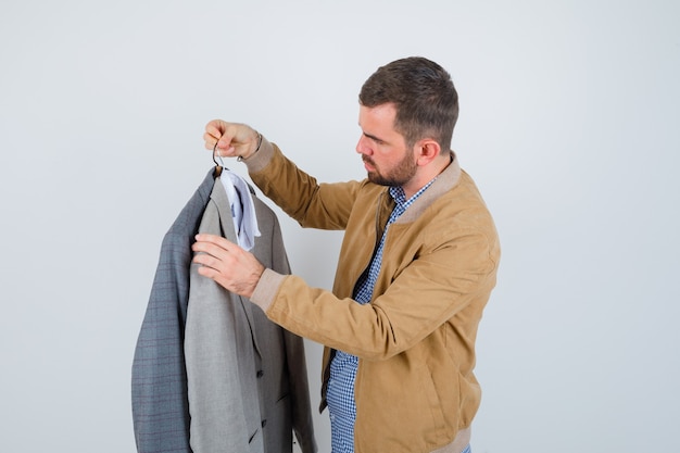 Giovane che guarda gli abiti, in piedi di lato in giacca, camicia e sembra serio.