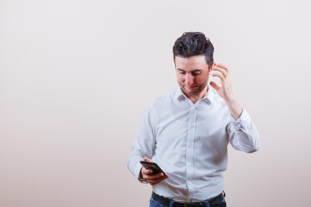 Giovane che guarda il cellulare mentre pensa in camicia, jeans e sembra irritato