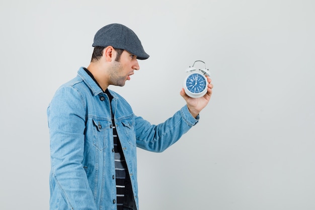 Giovane che guarda l'orologio in giacca, berretto e sembra eccitato. .