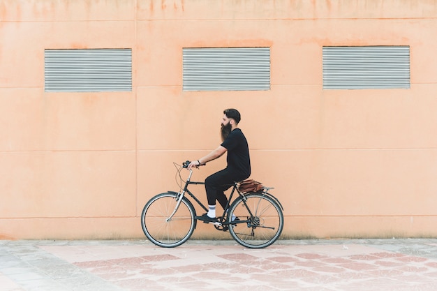 Giovane che guida la bicicletta davanti alla parete beige