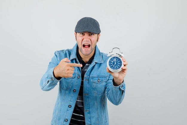 Giovane che indica all'orologio in giacca, berretto e che sembra nervoso.