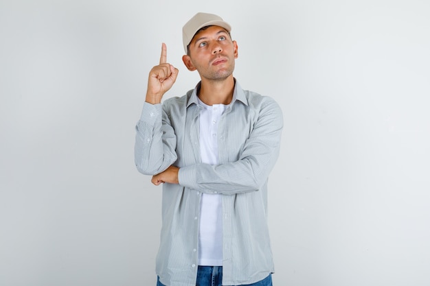 Giovane che indica il dito in t-shirt con cappuccio, jeans e guardando pensieroso