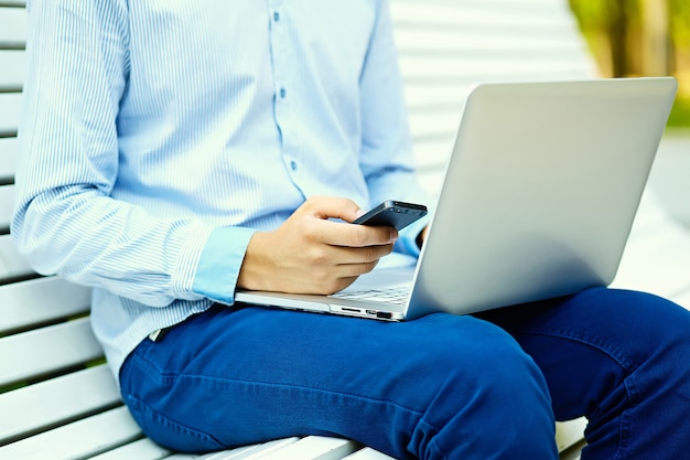 Giovane che lavora con il computer portatile, le mani dell'uomo sul computer portatile, uomo d'affari in abbigliamento casual in strada