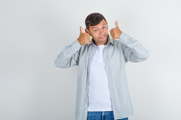 Giovane che mostra i pollici in su in camicia, jeans e che sembra contento