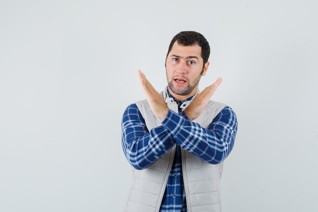 Giovane che mostra il gesto chiuso in camicia, giacca senza maniche e che sembra serio, vista frontale.