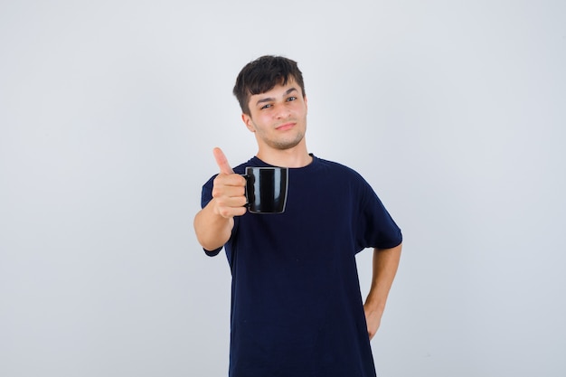 Giovane che offre una tazza di caffè in maglietta nera e sembra orgoglioso. vista frontale.