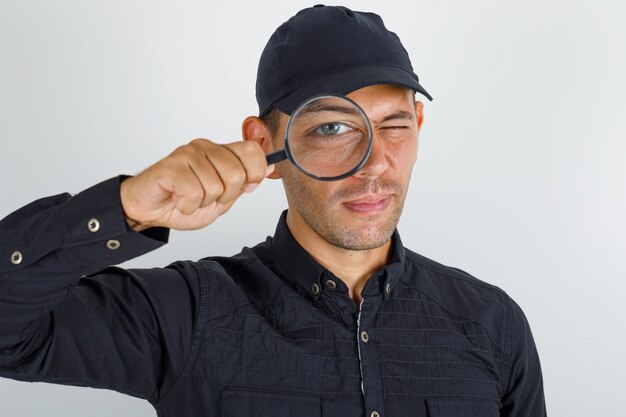 Giovane che osserva attraverso la lente d'ingrandimento in camicia nera con cappuccio