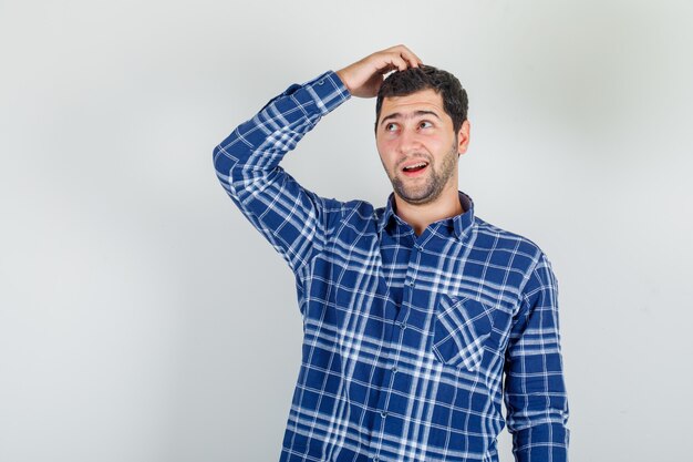 giovane che osserva in su con la mano sulla testa in camicia a quadri e sembra sognante.