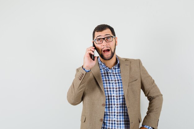 Giovane che parla sul telefono cellulare in camicia, giacca e guardando pensieroso