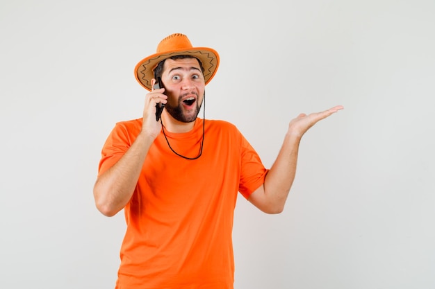 Giovane che parla sul telefono cellulare in maglietta arancione, cappello e che sembra felice. vista frontale.