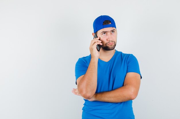 Giovane che parla sul telefono cellulare in maglietta blu e cappello e che sembra serio