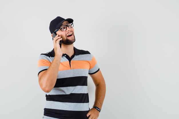 Giovane che parla sul telefono cellulare in t-shirt, cappello e sembra allegro