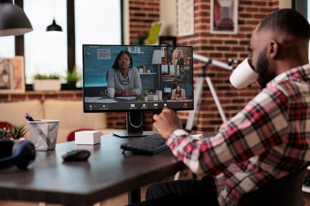 Giovane che partecipa a una riunione di videochiamata di lavoro con persone, utilizzando computer e webcam a casa. Lavorare in remoto su chiamate in teleconferenza online, parlare in chat in videoconferenza remota.