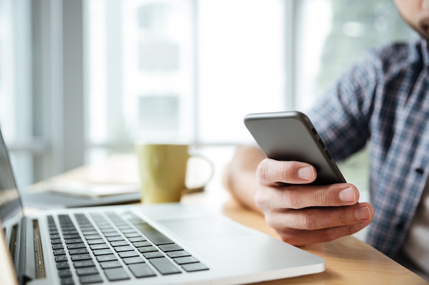 Giovane che per mezzo del computer portatile e del telefono.