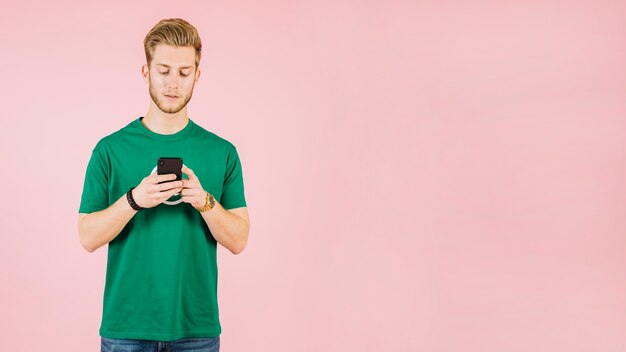 Giovane che per mezzo del telefono cellulare su fondo rosa