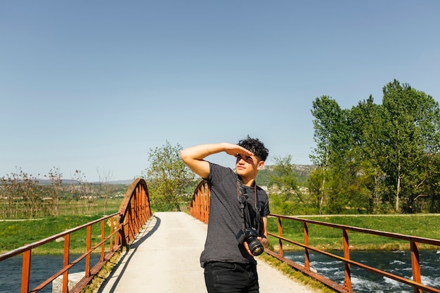 Giovane che protegge l&#39;occhio dalla luce del sole con la fotocamera