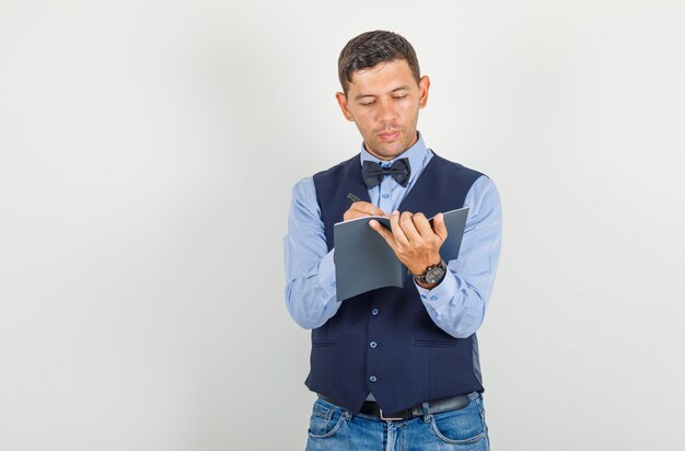 Giovane che scrive sul taccuino in vestito, jeans e che sembra occupato.