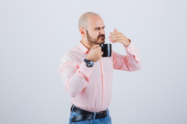 Giovane che sente un cattivo odore in camicia rosa, jeans e sembra disgustato. vista frontale.